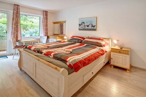Une chambre à coucher avec un lit, des tables de chevet, un bureau et une fenêtre avec des rideaux.