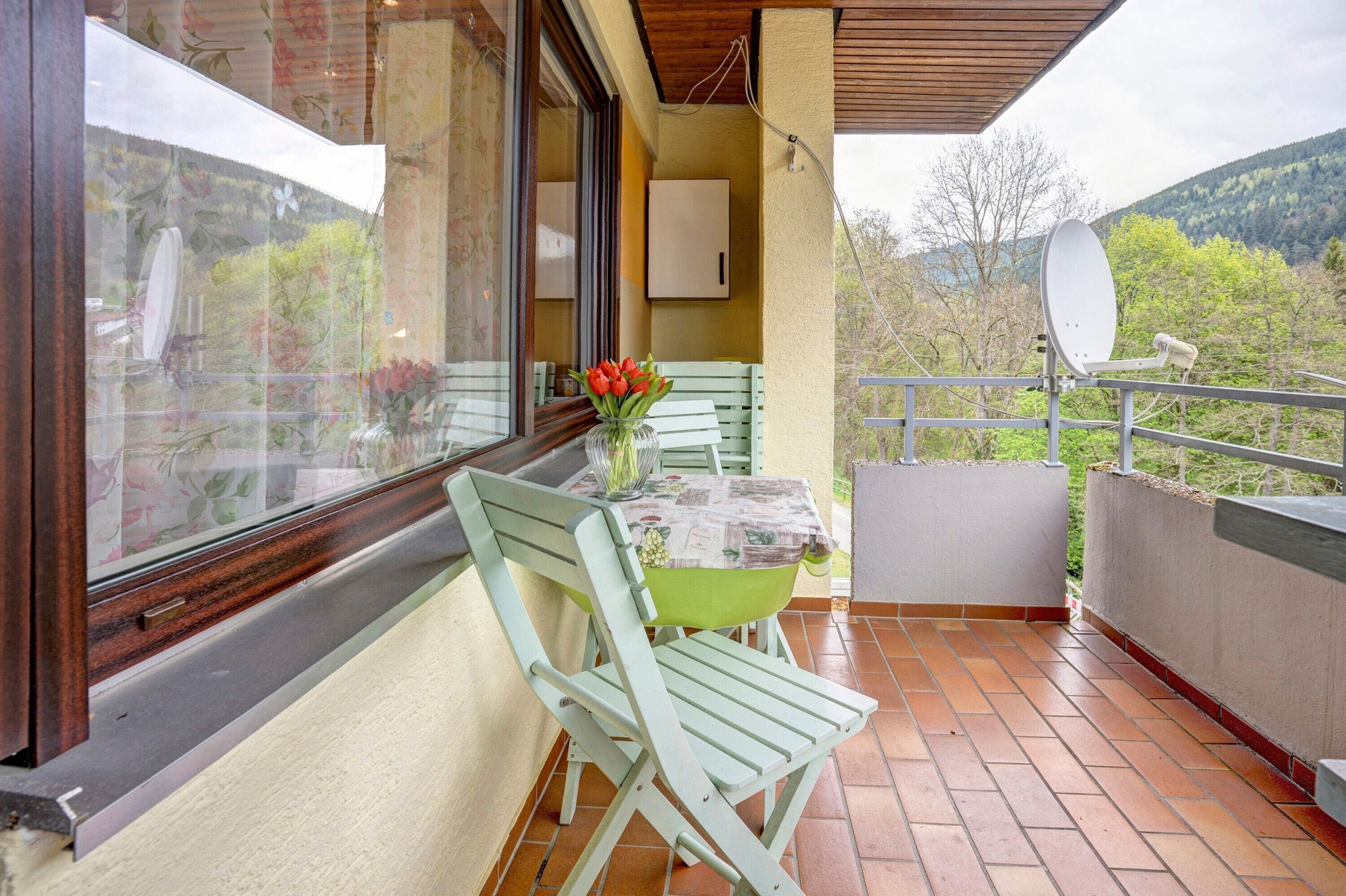 Een balkon met een tafel, stoelen, een bloevas en een schotelantenne.