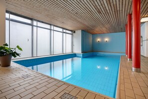 Une piscine intérieure dotée d’un sol carrelé, d’un plafond en bois et de grandes fenêtres.