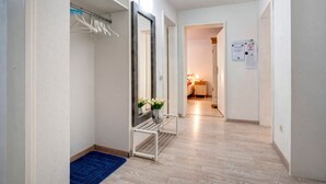 Un corridoio con un tappeto blu, una panca bianca, uno specchio e una porta che dà su una stanza con un letto e un comodino.