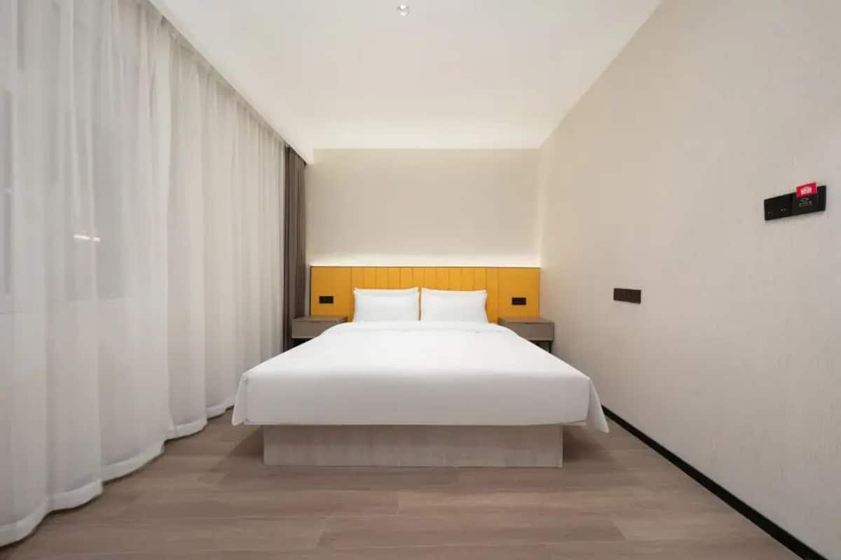 Habitación de hotel con una cama grande, cortinas blancas, un cabecero de madera y una mesita de noche.
