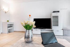 A modern living room with a laptop on a table, a TV, and a decorative vase with flowers. - Studio 'Tannenwald' with Balcony and Wi-Fi (Bad Wildbad)