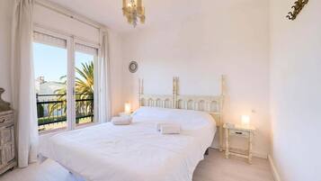 Una cama grande con sábanas blancas, un candelabro y una mesita de noche con lámpara.