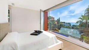 Un dormitorio con un ventanal grande, una cama y vistas a una piscina y vegetación.
