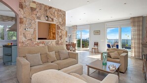 Uma sala de estar espaçosa com parede de pedra, um conjunto de sofá, mesa de centro e vista para o exterior.