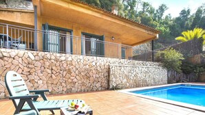 A poolside area with stone walls, a covered terrace, and outdoor furniture.