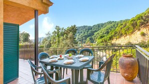 A terrace with a table set for dining, overlooking a lush green hillside.