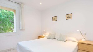 A bedroom with a large bed, two bedside tables, a window with curtains, and two framed pictures on the wall.