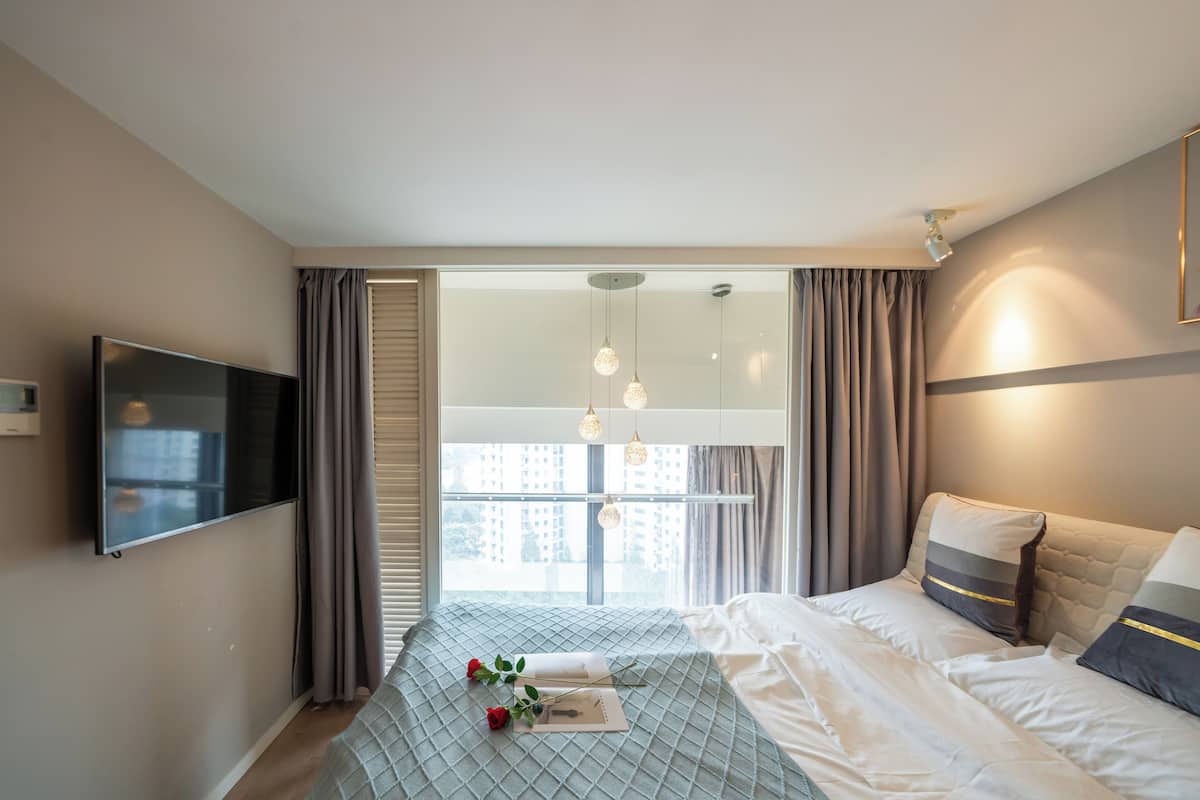 A modern bedroom with a large bed, a flat-screen TV, and a window with curtains.