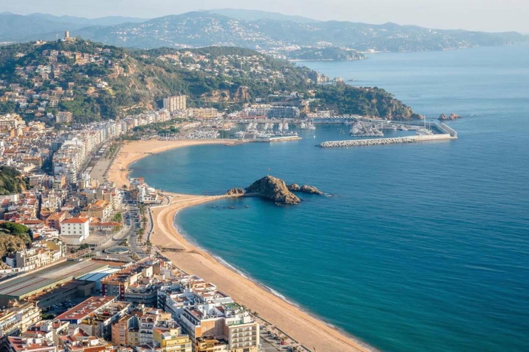 Un paysage urbain côtier avec une plage, des bâtiments et un promontoire rocheux qui s’avance dans l’eau.