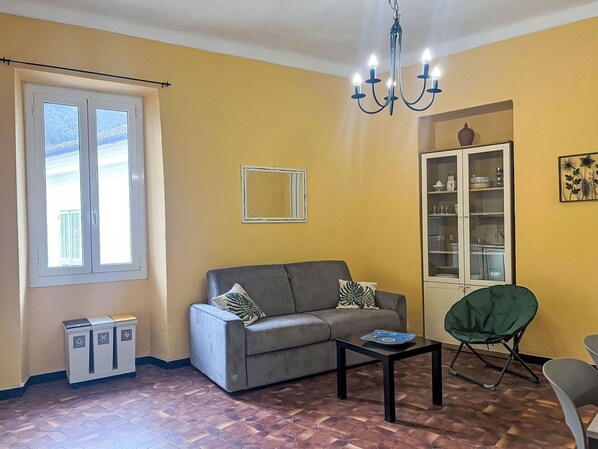 A living room with a sofa, a coffee table, a chair, a cabinet, and a trash bin.