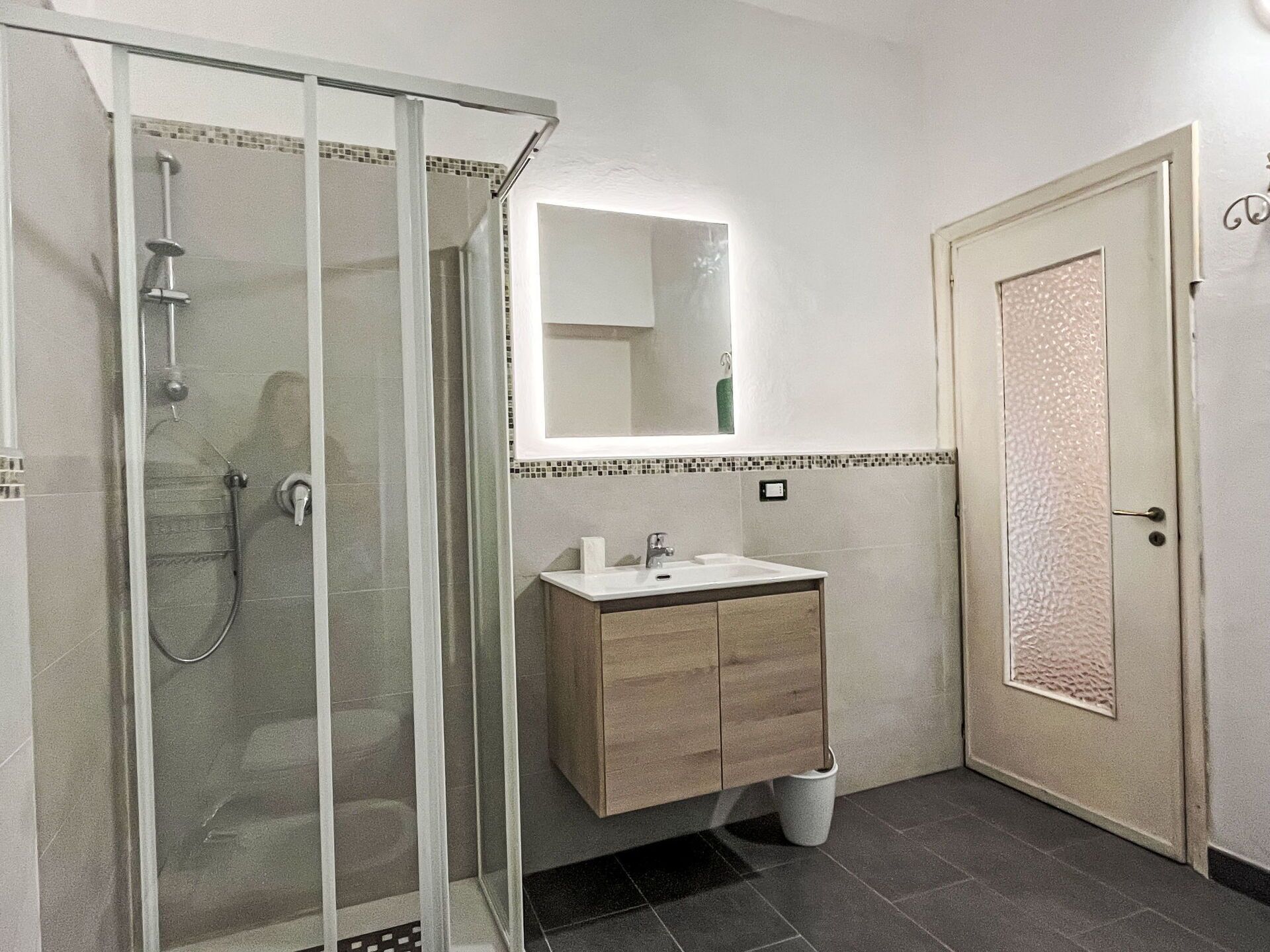 A bathroom with a glass-enclosed shower, a sink with a mirror above it, and a door with a textured pattern.