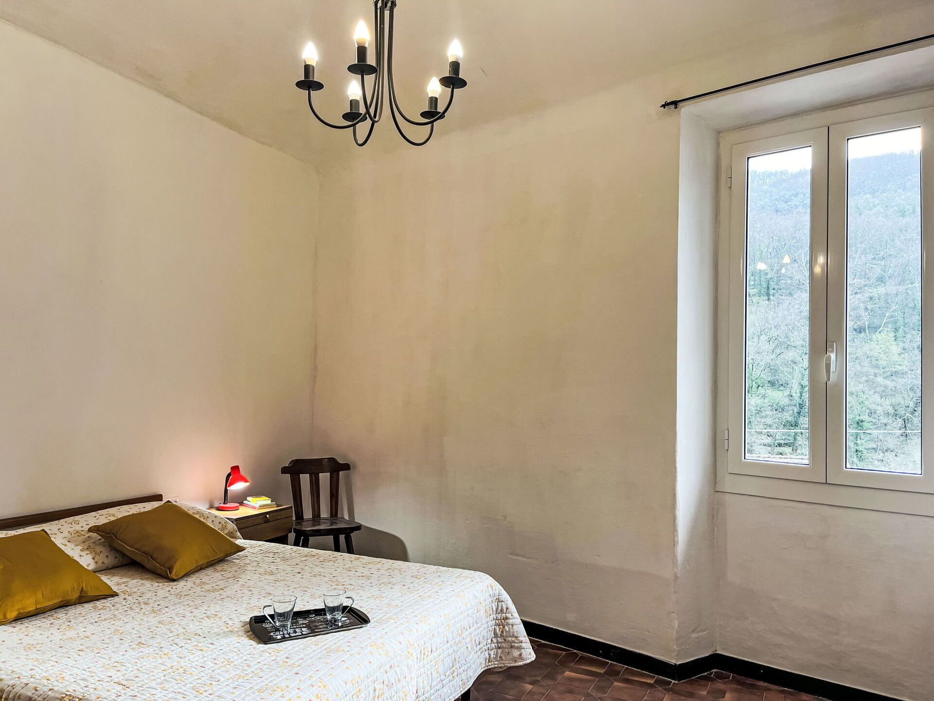 Une chambre à coucher comprenant un lit, une table de chevet, une chaise, une fenêtre donnant sur un beau paysage et un lustre.