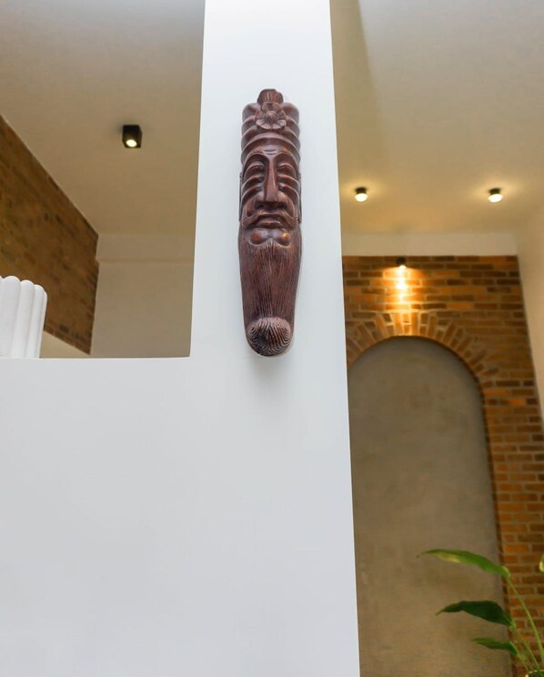 A wooden carved wall piece in a room with a brick wall and white ceiling. - Rome Transit Hotel (Negombo)