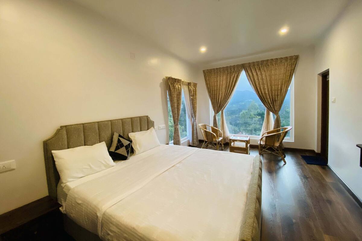 Une chambre avec un grand lit, deux fauteuils et une vue sur l’extérieur.