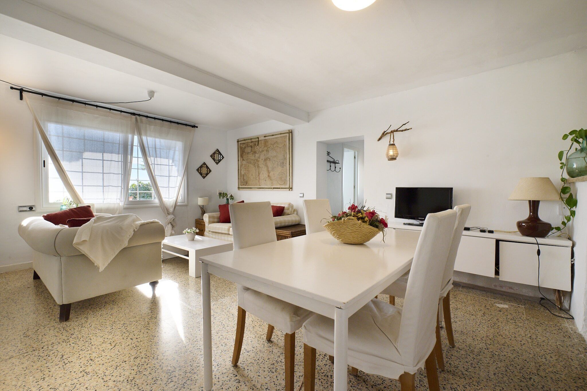 Una sala de estar moderna con un sofá blanco, una mesa de comedor con sillas, un televisor y una lámpara.