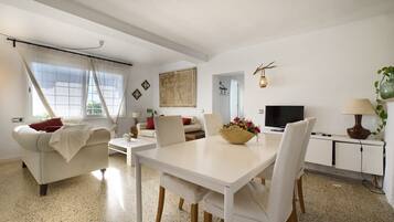 Una sala de estar moderna con un sofá blanco, una mesa de comedor con sillas, un televisor y una lámpara.
