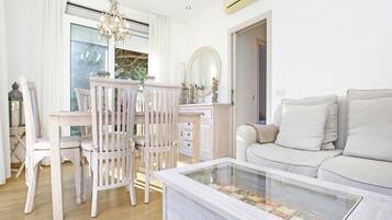 Una sala de estar con un sofá blanco, una mesa de centro de vidrio y una mesa de comedor de madera con sillas.