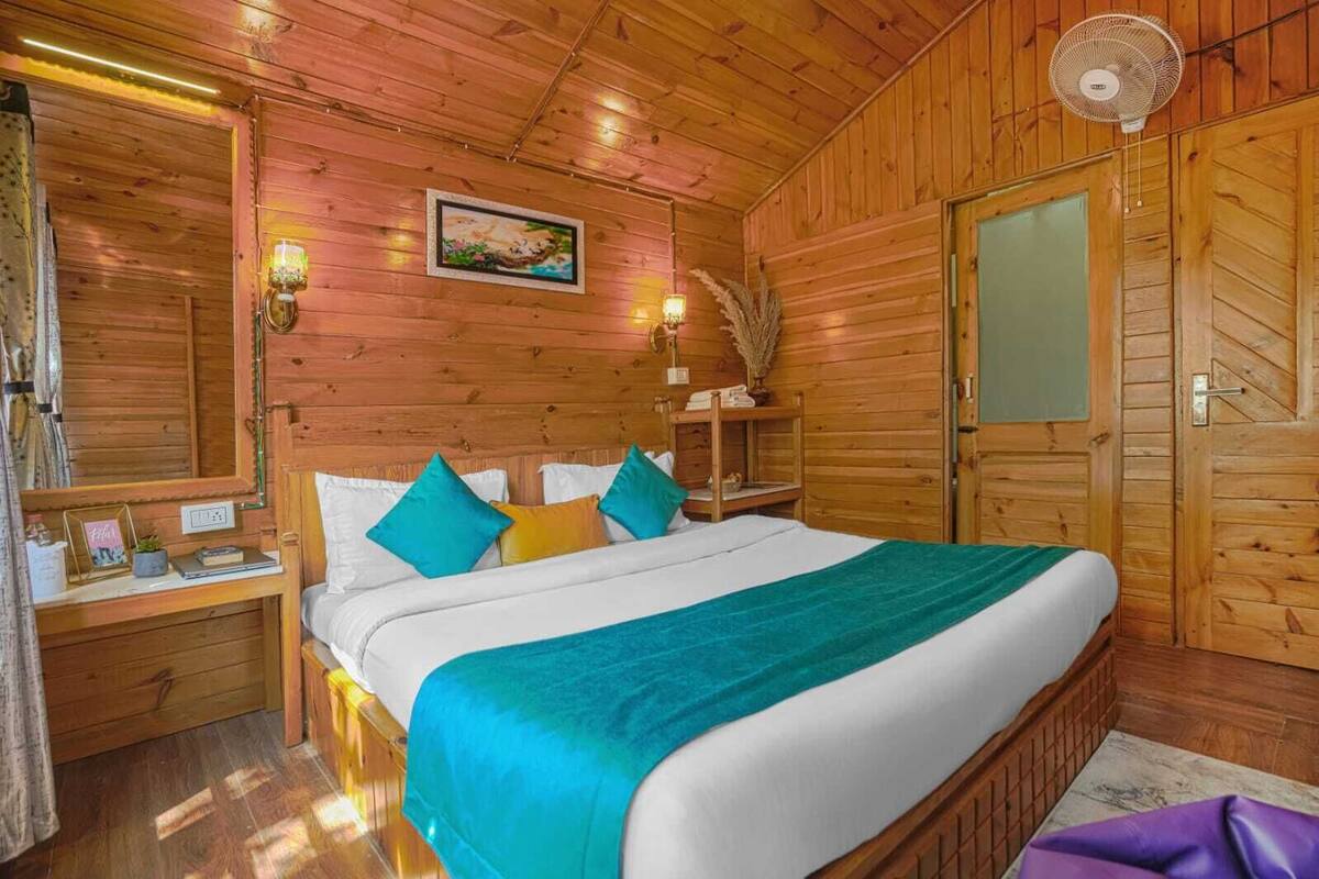 Un dormitorio tipo cabaña de madera con cama, mesitas de noche, un espejo y un ventilador.
