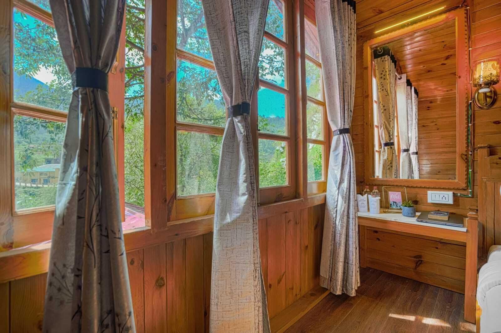 A wooden cabin room with large windows, a wooden dresser, and a mirror.