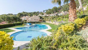 A swimming pool surrounded by greenery and a hillside with houses. - Villa in Llafranc with Sea Views & Pool (Llafranc)