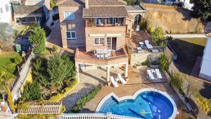 A two-story house with a swimming pool, a covered patio, and a garden.