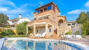 A two-story house with a stone facade, a swimming pool, and outdoor seating.