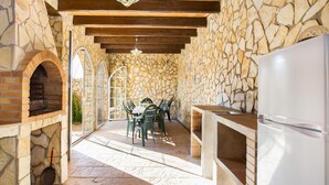 An outdoor patio with stone walls, a brick oven, and a dining table with chairs.