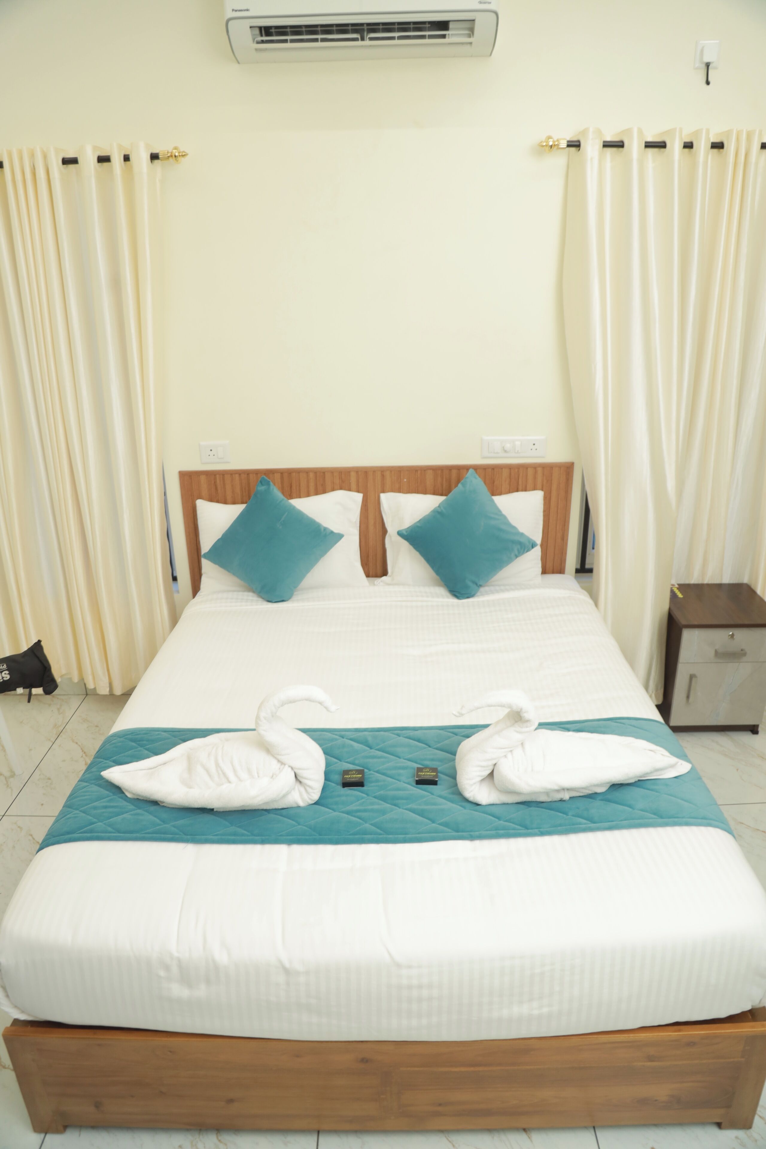 A neatly made bed with a wooden headboard, two pillows, and a swan-shaped towel arrangement.