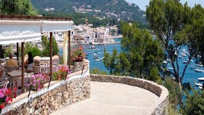 A seaside terrace with stone walls, outdoor seating, and a view of boats and buildings across the water. - Apartment in Llafranc near Beach & Pool (Llafranc)