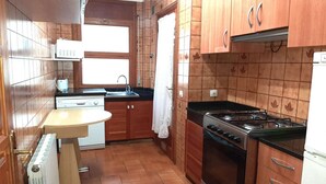 A compact kitchen with wooden cabinets, a gas stove, a built-in oven, a white countertop, and a window above the sink.
