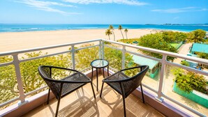 Un balcón con dos sillas y una mesa con vista a una playa y el océano.