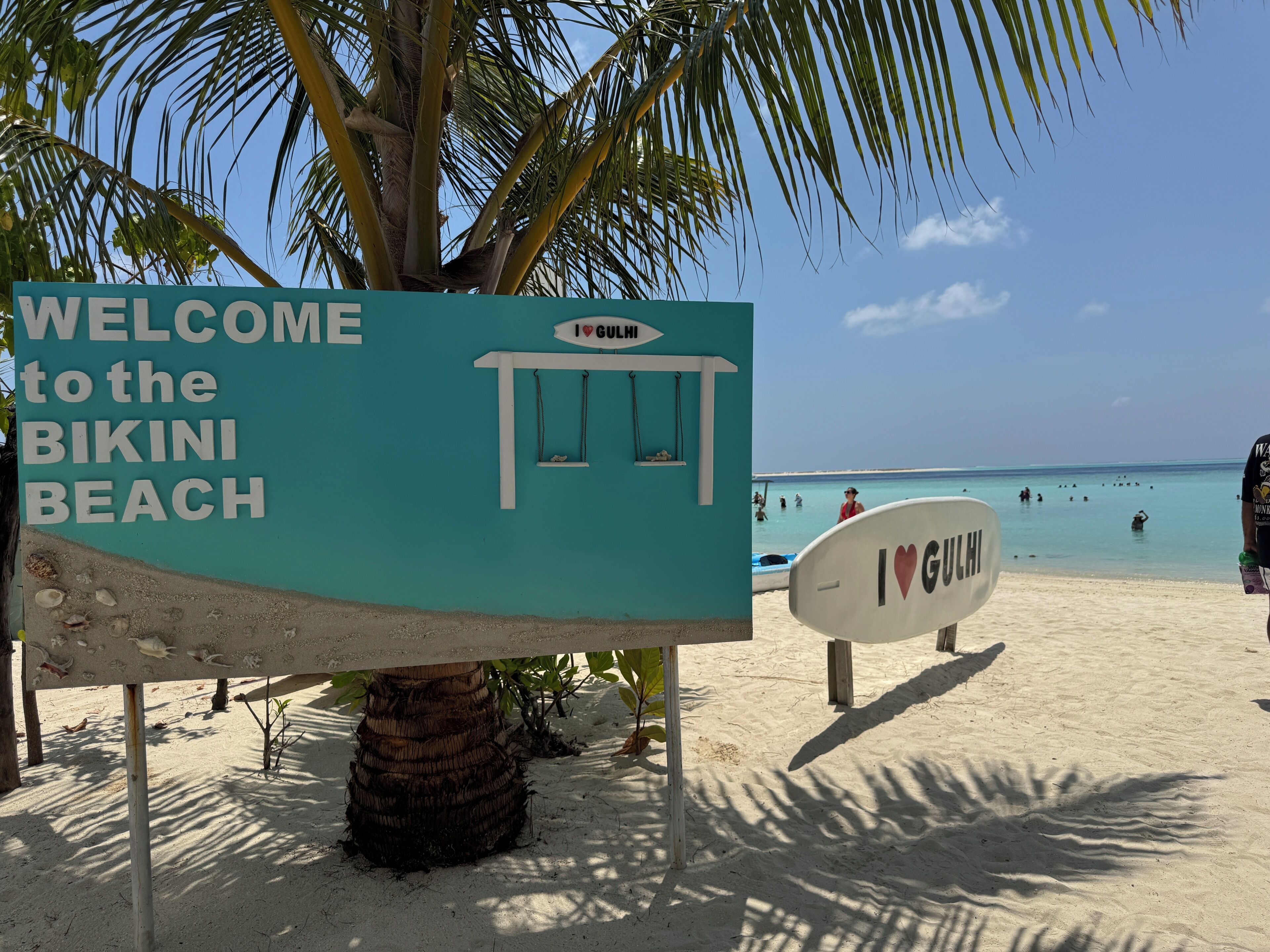 A beach sign welcoming visitors to Bikini Beach with a small kiosk and a lifeguard tower.
