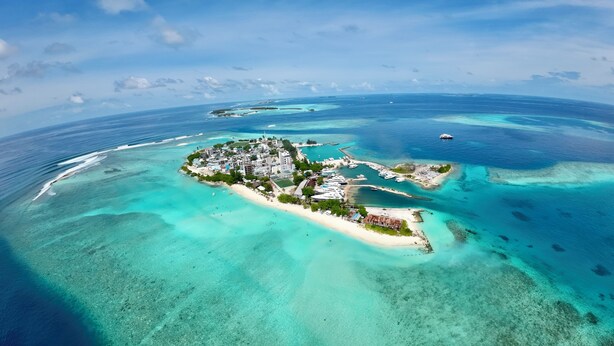 Vista aérea de una isla tropical con aguas turquesas cristalinas, un complejo de edificios centrales y un puerto deportivo con barcos.