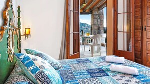 Een slaapkamer met een bed, kussens en uitzicht op een balkon met een tafel en stoelen.