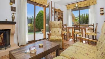 Un salon avec une cheminée, un coin repas avec des meubles en bois et de grandes fenêtres avec des rideaux.