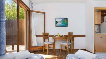 Une pièce avec deux lits, une table en bois avec des chaises, un tableau au mur et un coin cuisine.