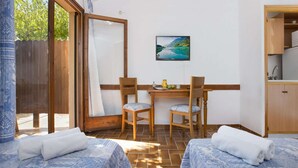 Ein Zimmer mit zwei Betten, einem Holztisch mit Stühlen, einem Bild an der Wand und einer Küchenzeile.