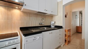 A modern kitchen with white cabinets, a black countertop, a built-in stove, a dishwasher, and a coffee maker.