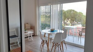 Un comedor moderno con una mesa redonda, sillas blancas y vistas a un balcón con barandilla y vegetación.