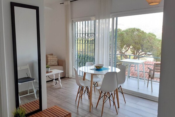 Un comedor moderno con una mesa redonda, sillas blancas y vistas a un balcón con barandilla y vegetación.