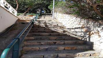Una escalera de piedra con barandales de metal, rodeada de follaje y un muro de piedra.