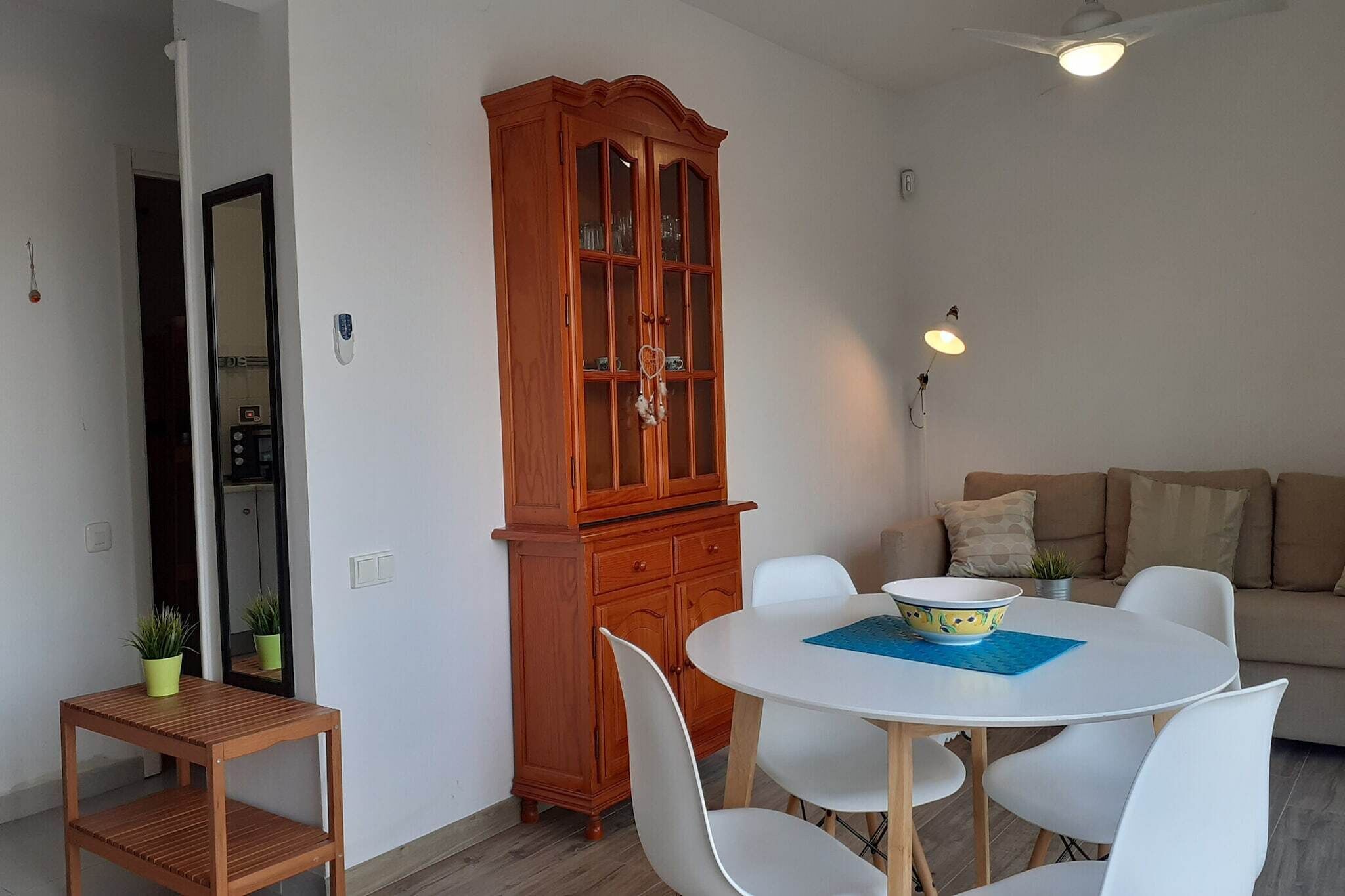 Un coin repas comprenant une table ronde blanche, des chaises blanches, un meuble en bois et un canapé.
