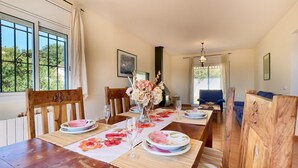A dining area with a wooden table set for four, chairs, and a vase of flowers. - Villa on Costa Brava with Pool & Sea Views (Lloret de Mar)