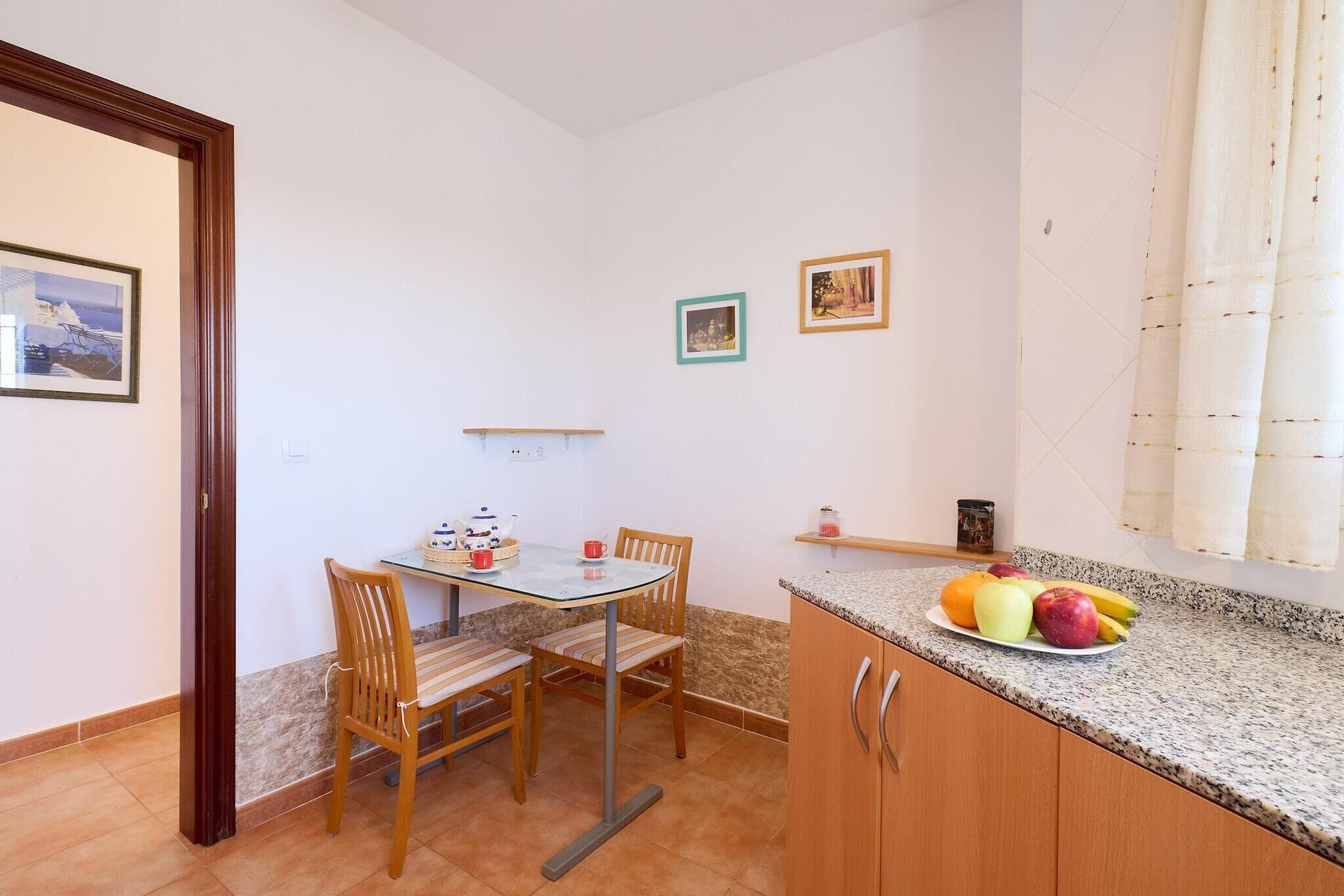 A small kitchen with a dining table, chairs, and a fruit bowl on the counter.