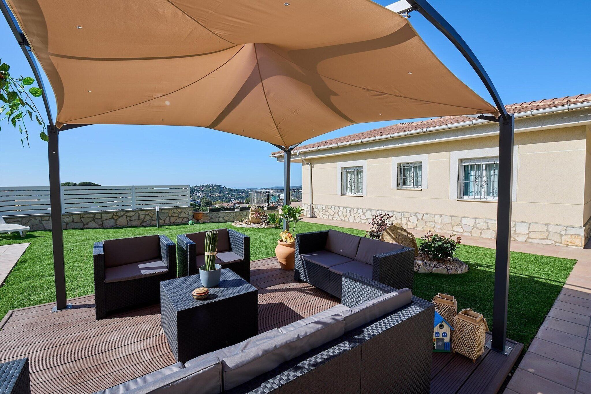A covered outdoor seating area with wicker furniture and a tan canopy, overlooking a well-maintained lawn and a stone wall.