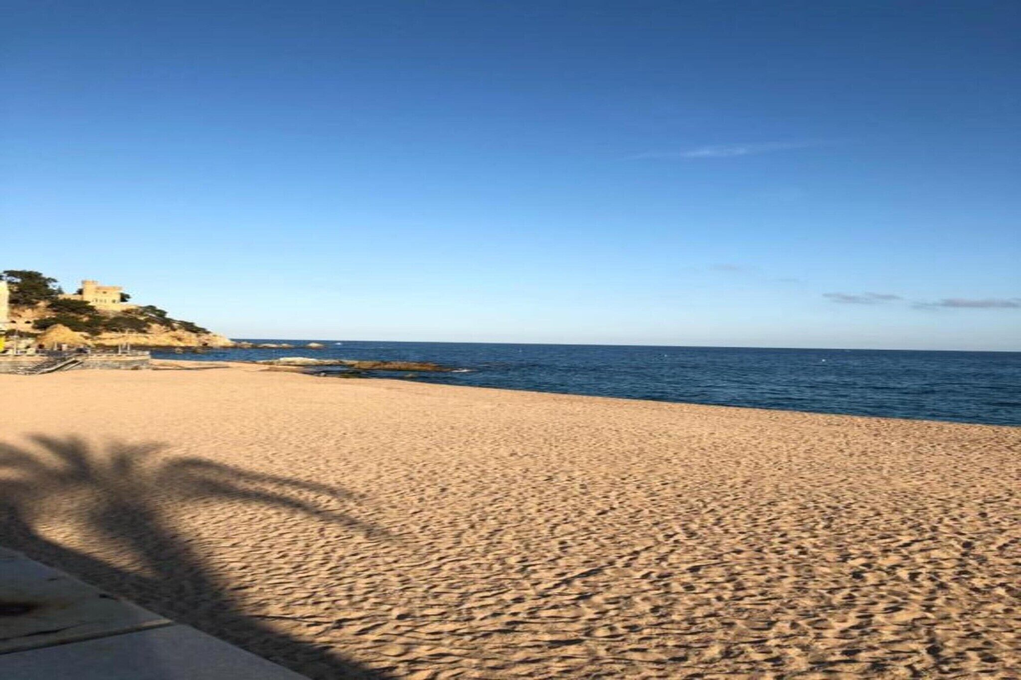 Una playa arenosa con cielo despejado y un edificio en la distancia sobre un acantilado.