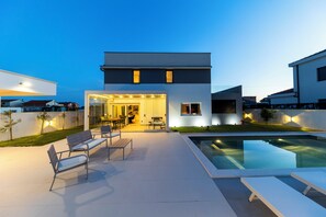 Une maison moderne dotée d’une piscine, d’un espace salon extérieur et d’une entrée bien éclairée.
