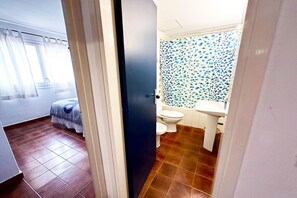 Une salle de bain avec un carrelage au sol, des toilettes, un lavabo et un espace douche agrémenté d’un rideau de douche à pois bleus et blancs.