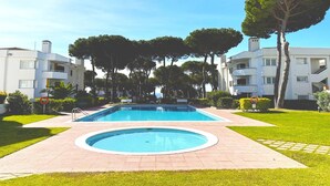 A swimming pool surrounded by a well-maintained lawn and trees, with modern buildings in the background. - Apartment in Spain near Beaches & City Center (Calella de Palafrugell, Llafranc)